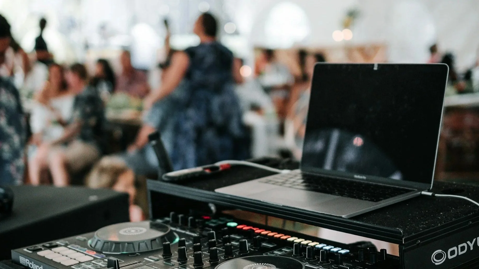 DJ setup with laptop and controller at a private celebration with guests in the background.