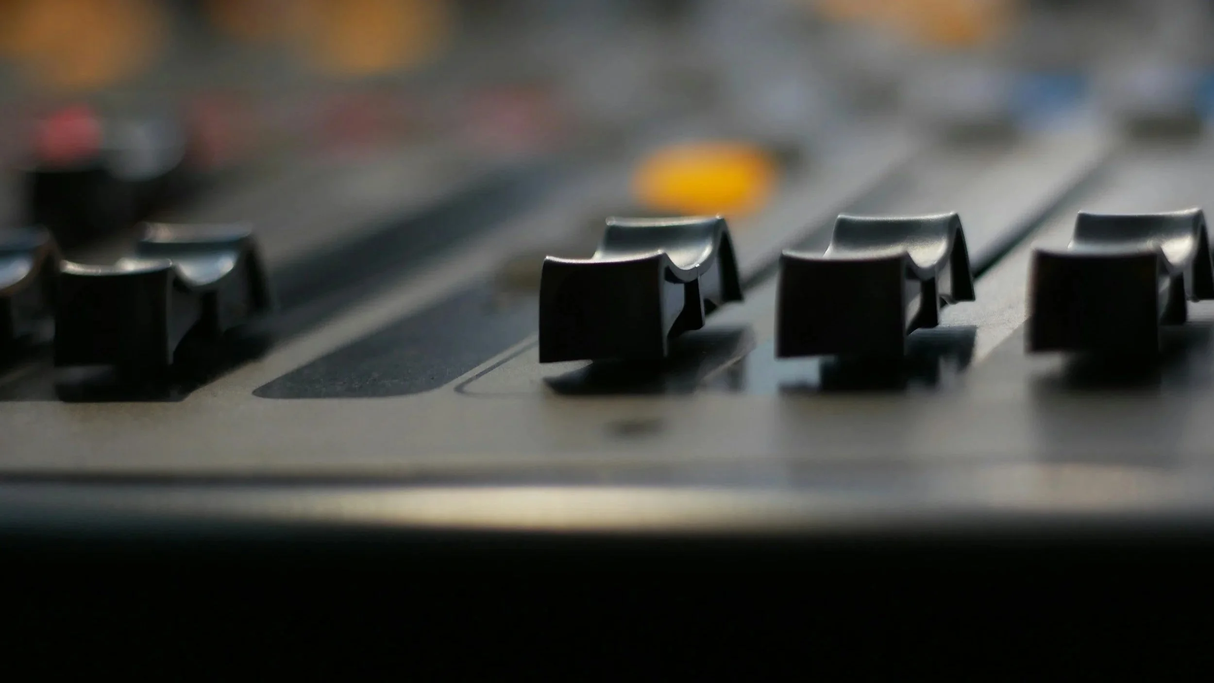 Close-up of an audio mixing console with faders and rotary controls.