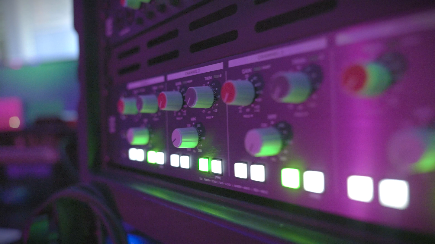 Close-up of professional rack-mounted audio equipment with illuminated controls in a recording setup.