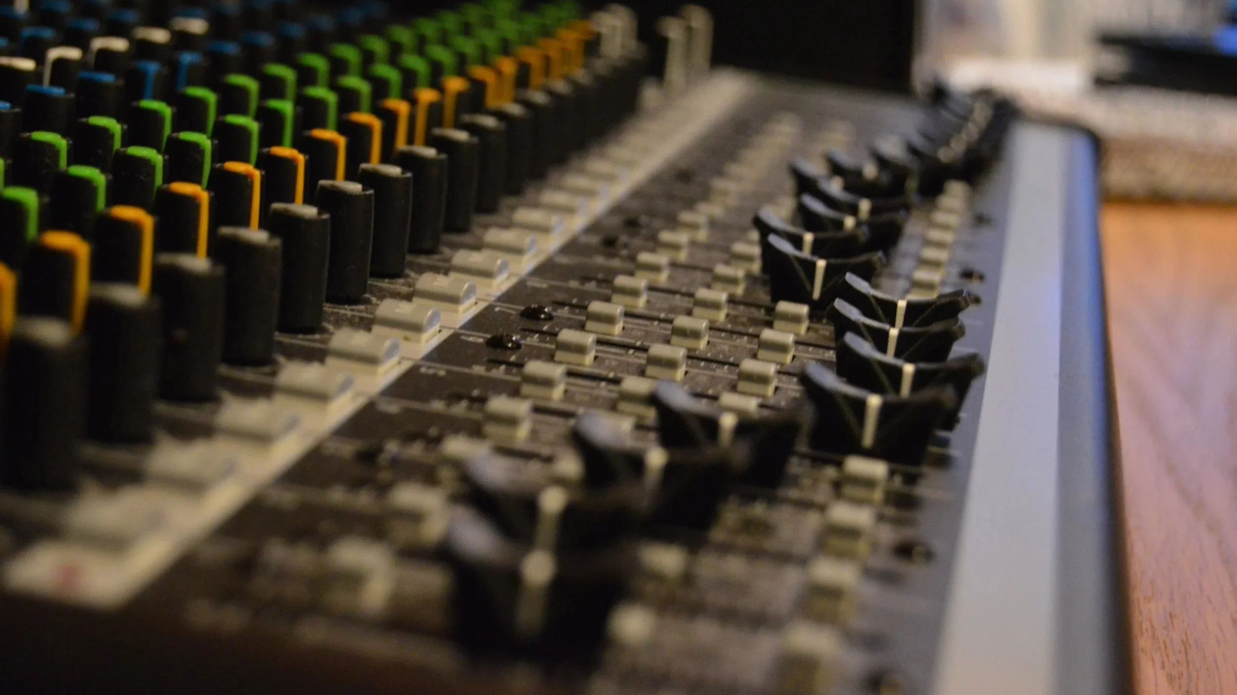 Close-up of a professional audio mixing console with rows of faders and rotary controls.