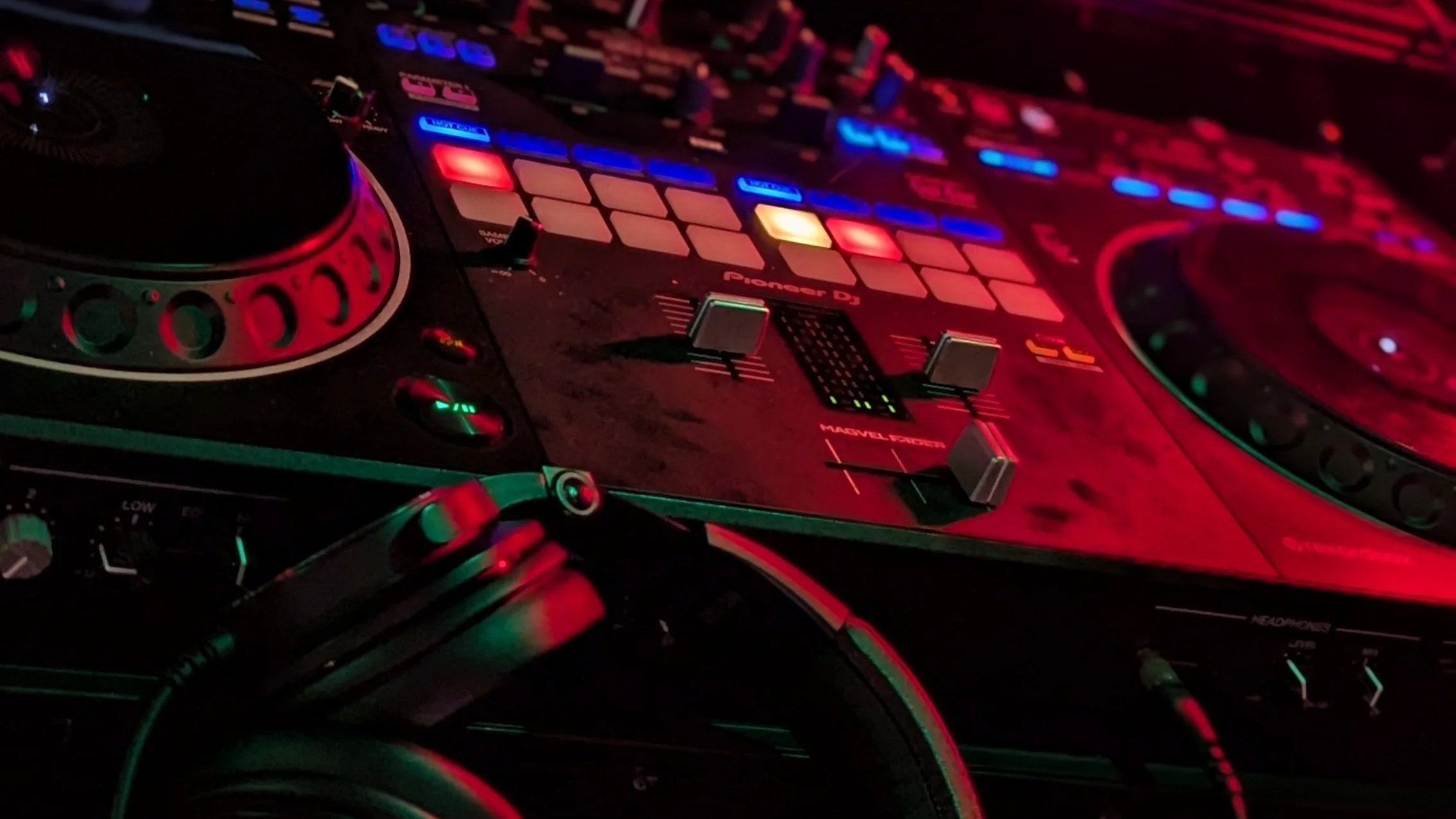 DJ controller and turntable equipment illuminated by colorful event lighting.