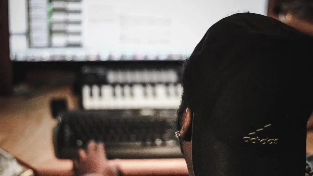 Music producer working at a studio workstation with audio equipment and computer screens.