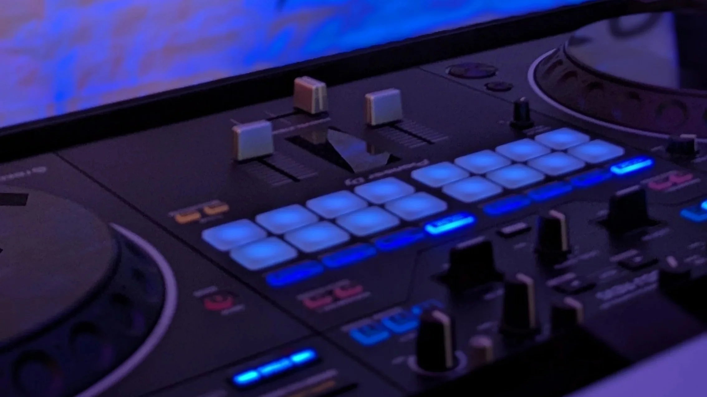 Close-up of a DJ controller with illuminated performance pads and controls.