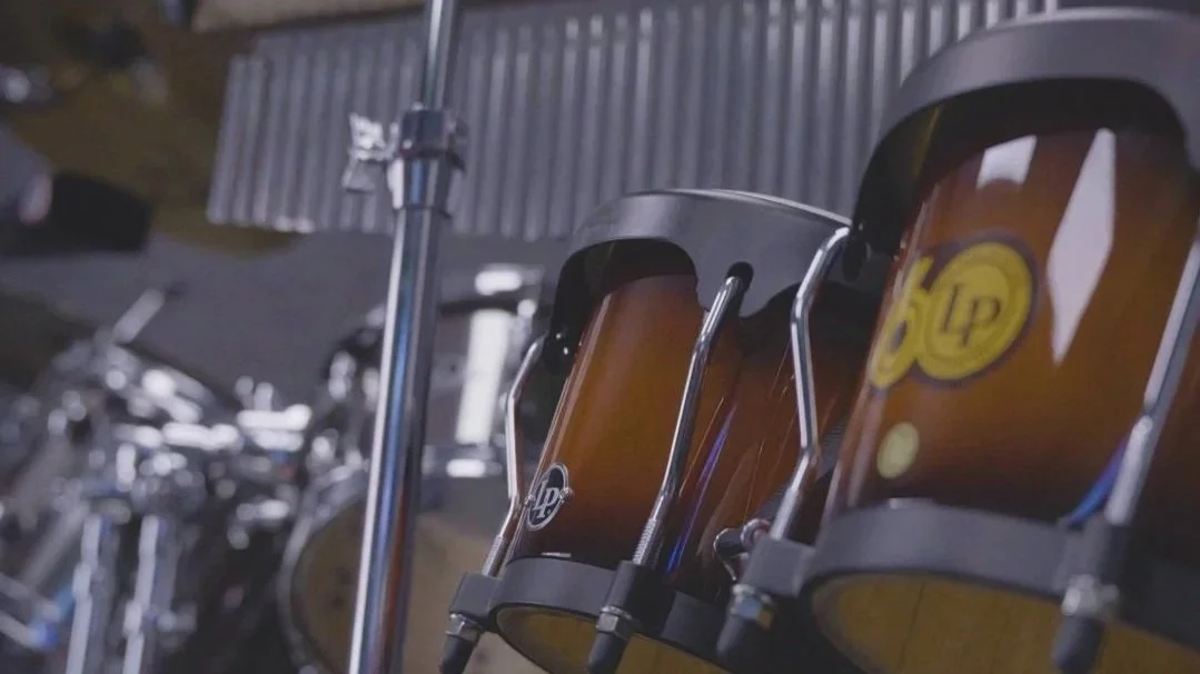 Congas on stands beside a microphone stand and drum hardware.