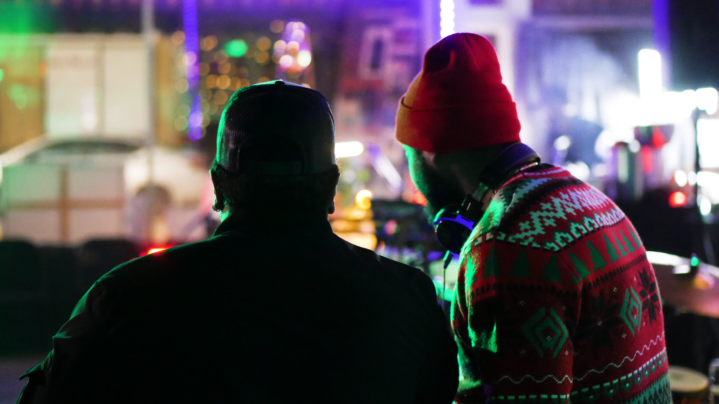 Two people working together during a behind-the-scenes production setup with colorful lighting.
