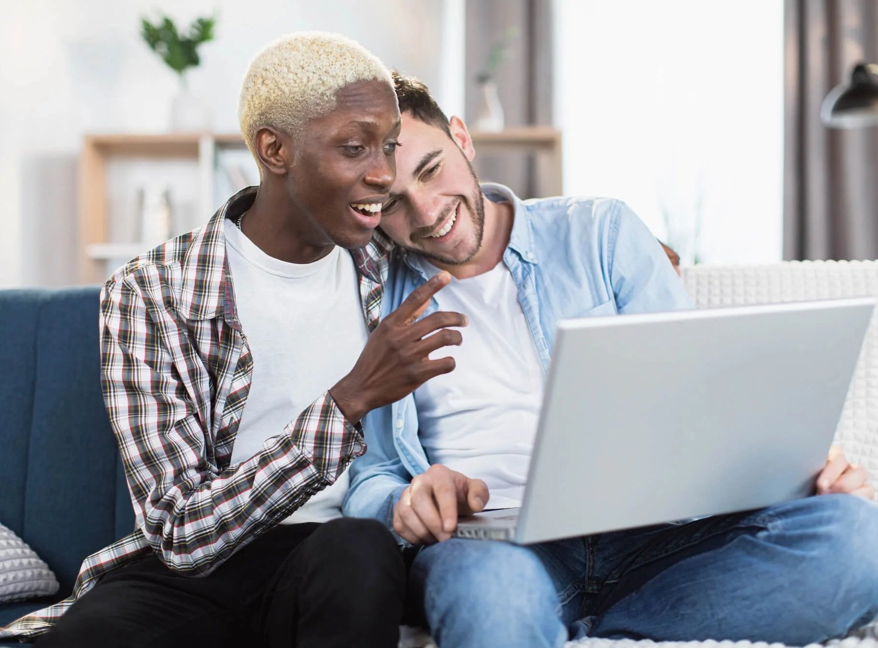 Gay interracial couple using a laptop together, representing connection and support through LGBTQ+ affirming therapy in Atlanta.