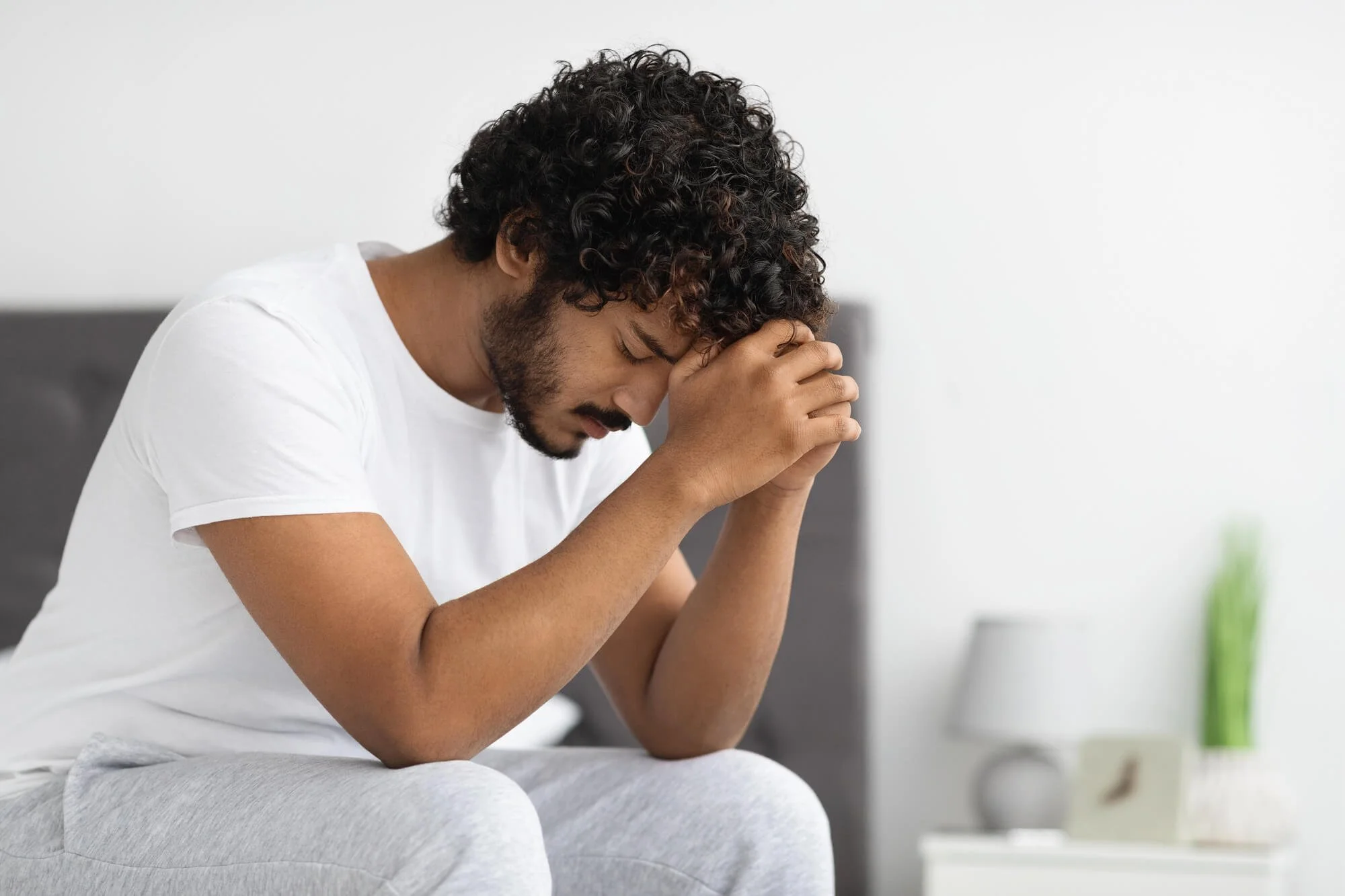 Young adult sitting alone with his head down, showing emotional distress that may be connected to addiction or recovery challenges.