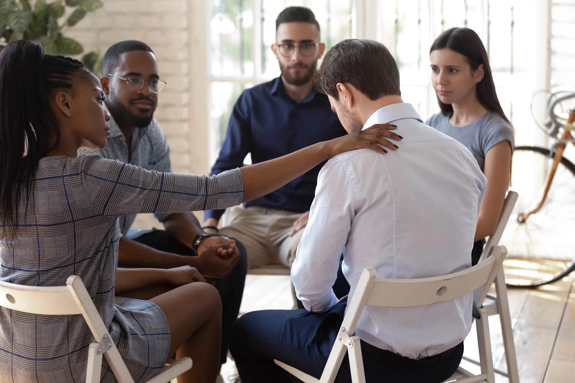 Adults in an addiction recovery counseling group supporting a participant during a therapy session.