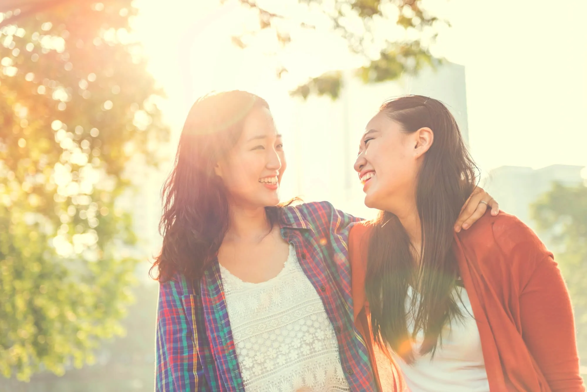 Asian LGBTQ+ couple smiling together outdoors, representing connection and support through LGBTQ+ affirming therapy in Atlanta.