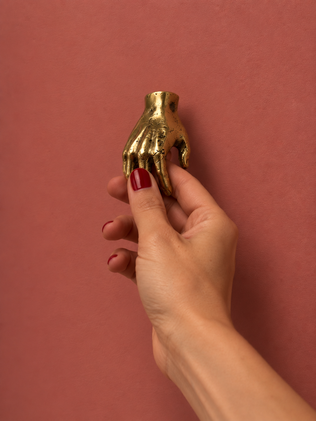 Une main saisit la poignée sculpturale HANDY en laiton, sur fond rose.