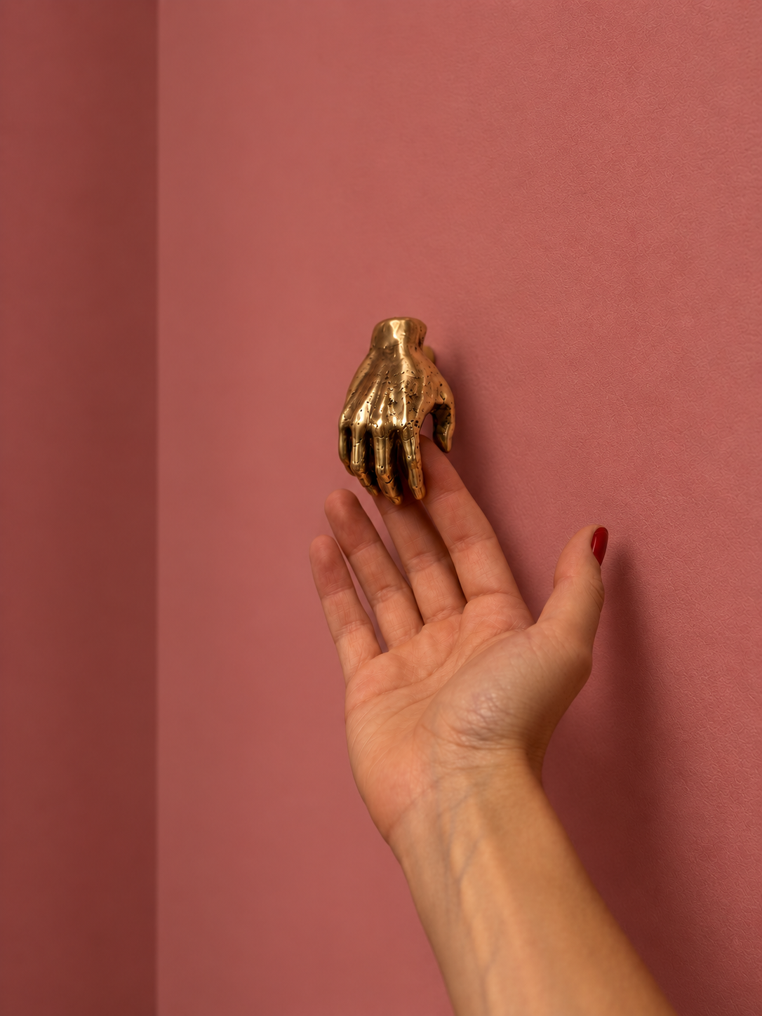 Petite poignée HANDY en laiton au-dessus d’une paume ouverte, sur fond rose.