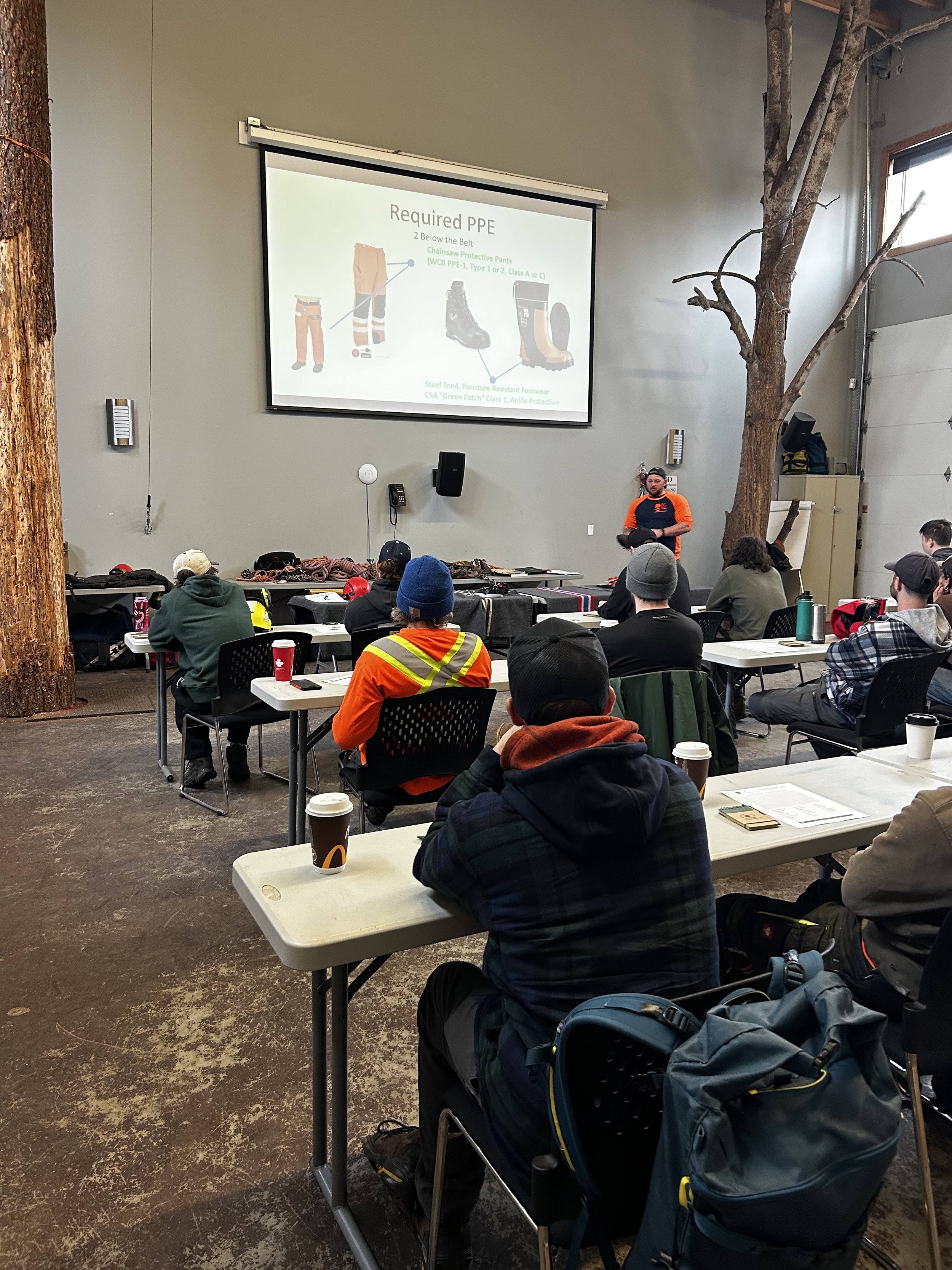 Arborists attending an in-person safety training course at the BCPHC training facility in Surrey, BC, with instructor presenting required PPE standards.