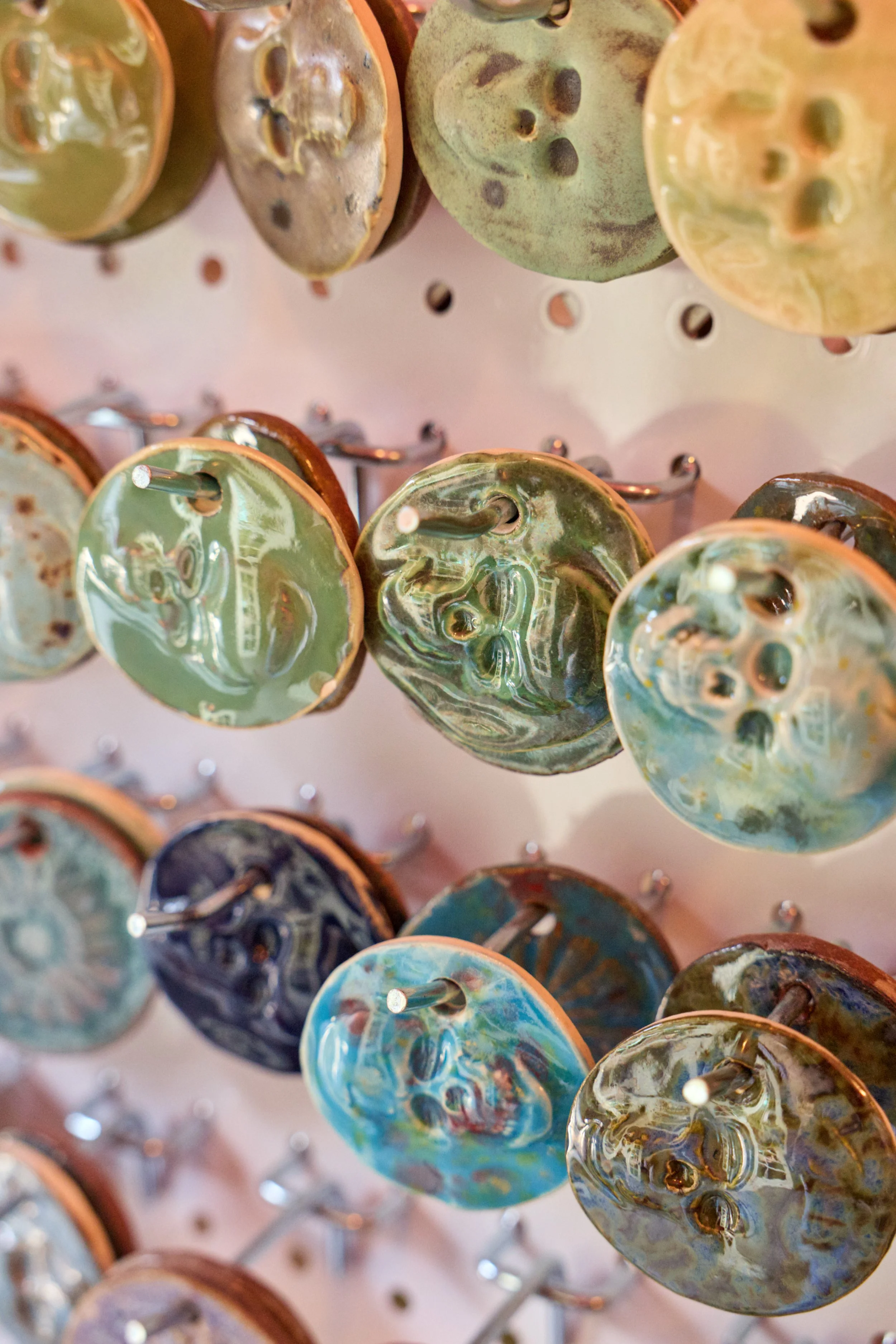 Close-up of various colorful ceramic cup handles hanging on a display rack with metal hooks.
