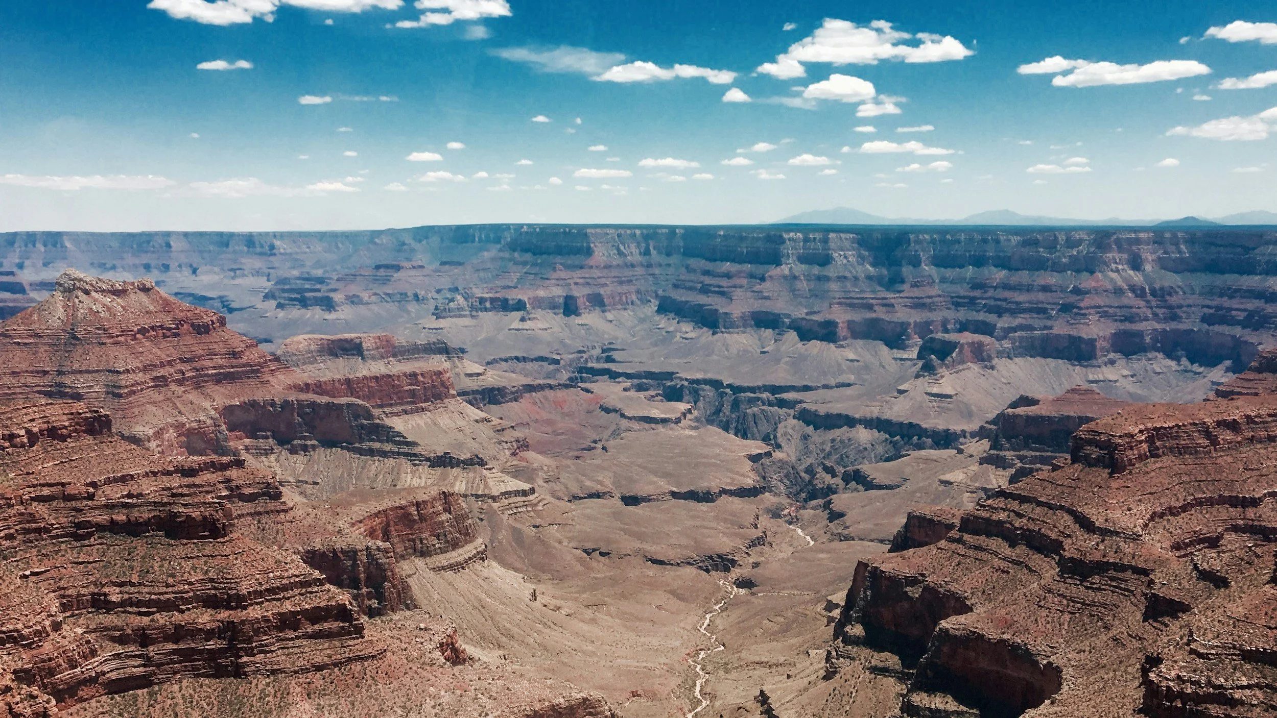 Landscape shot of desert canyons underneath a blue sky with some clouds.