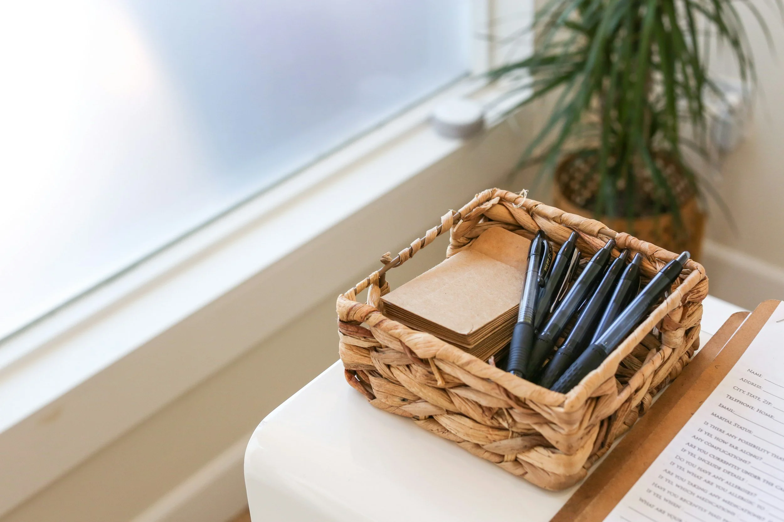 Wicker basket with black pens and brown sheets of paper on a sofa in a room.