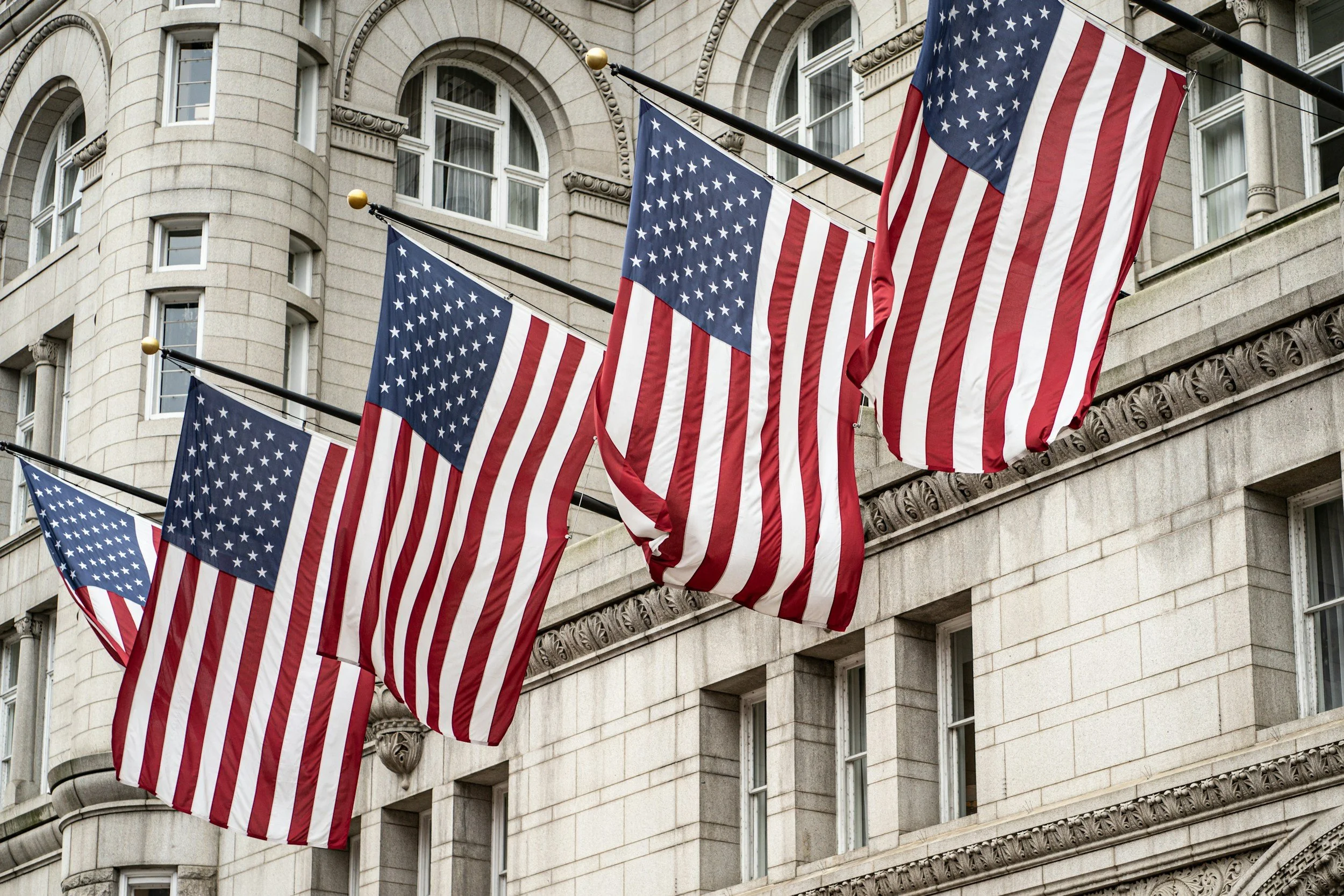 Row of American flags on poles attached to large building.