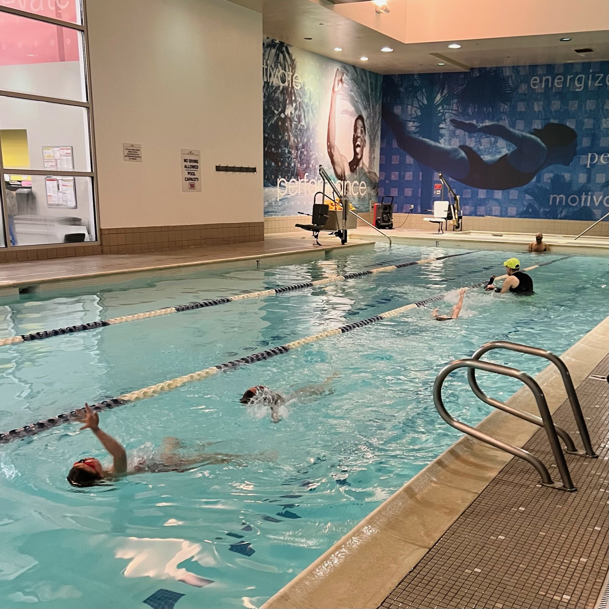 Four students swim in a lap lane with a coach assisting.