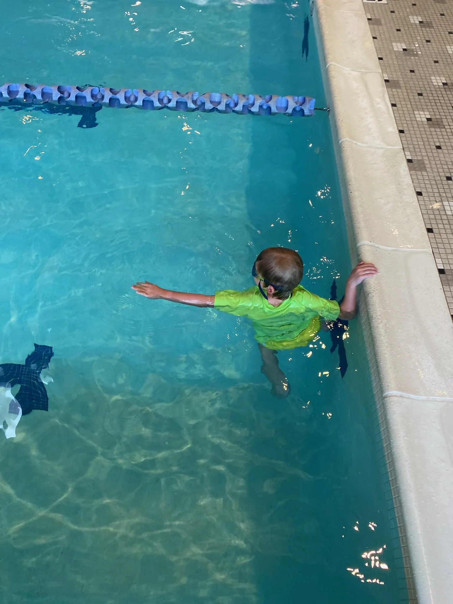 Child in a pool, holding a wall and preparing to swim.