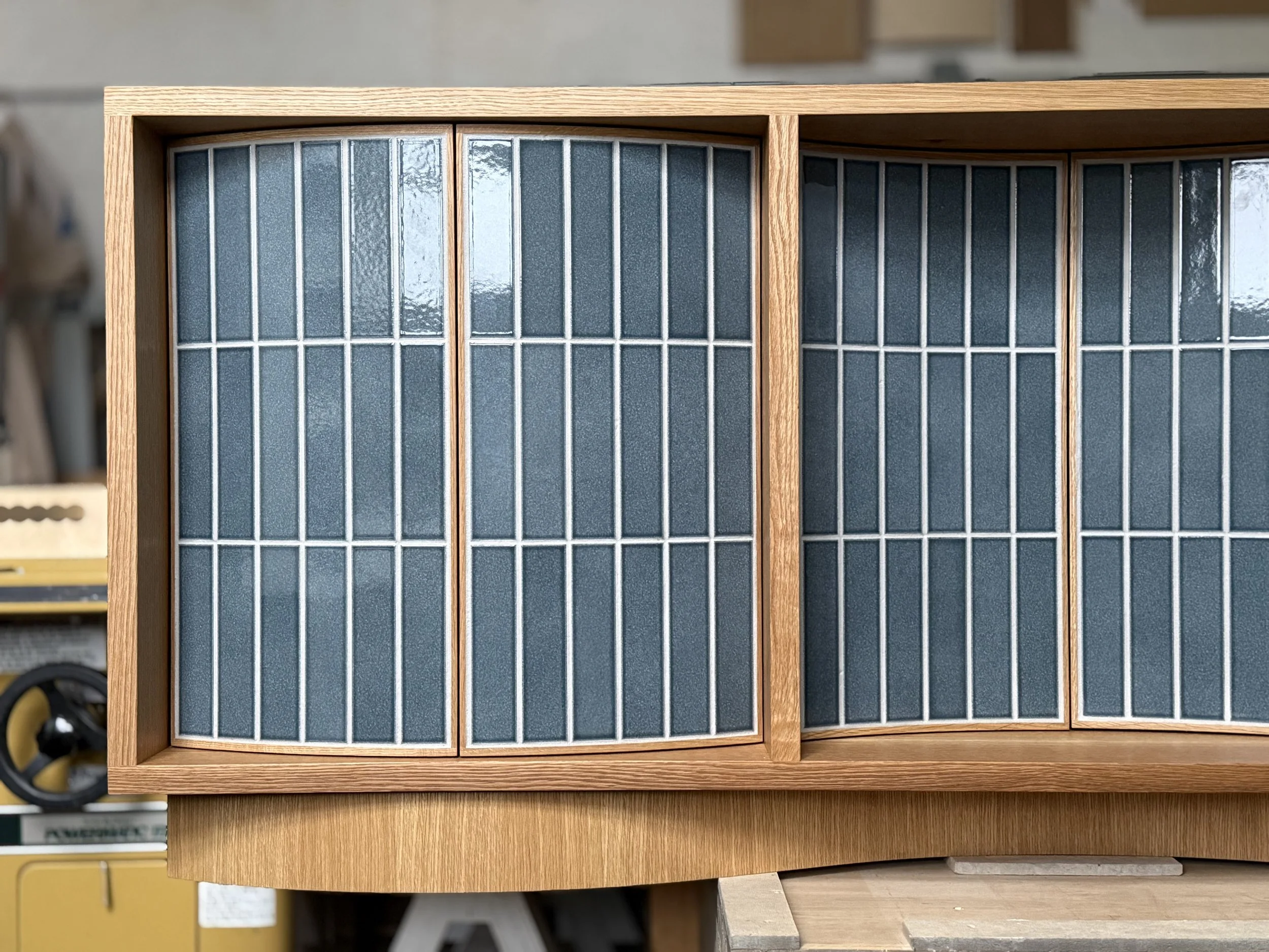 A wooden cabinet with Nagano Blue ceramic tile paneled doors in a workshop setting. Custom furniture.  Handcrafted by Milk Furniture LLC in Rhode Island.