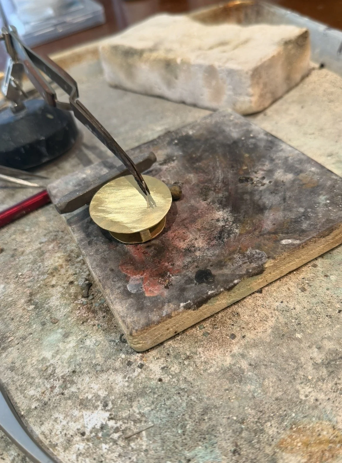 Brass disc being soldered on fire brick at Frog Aspect Brooklyn studio — handmade brass art jewelry by Einat Cohen