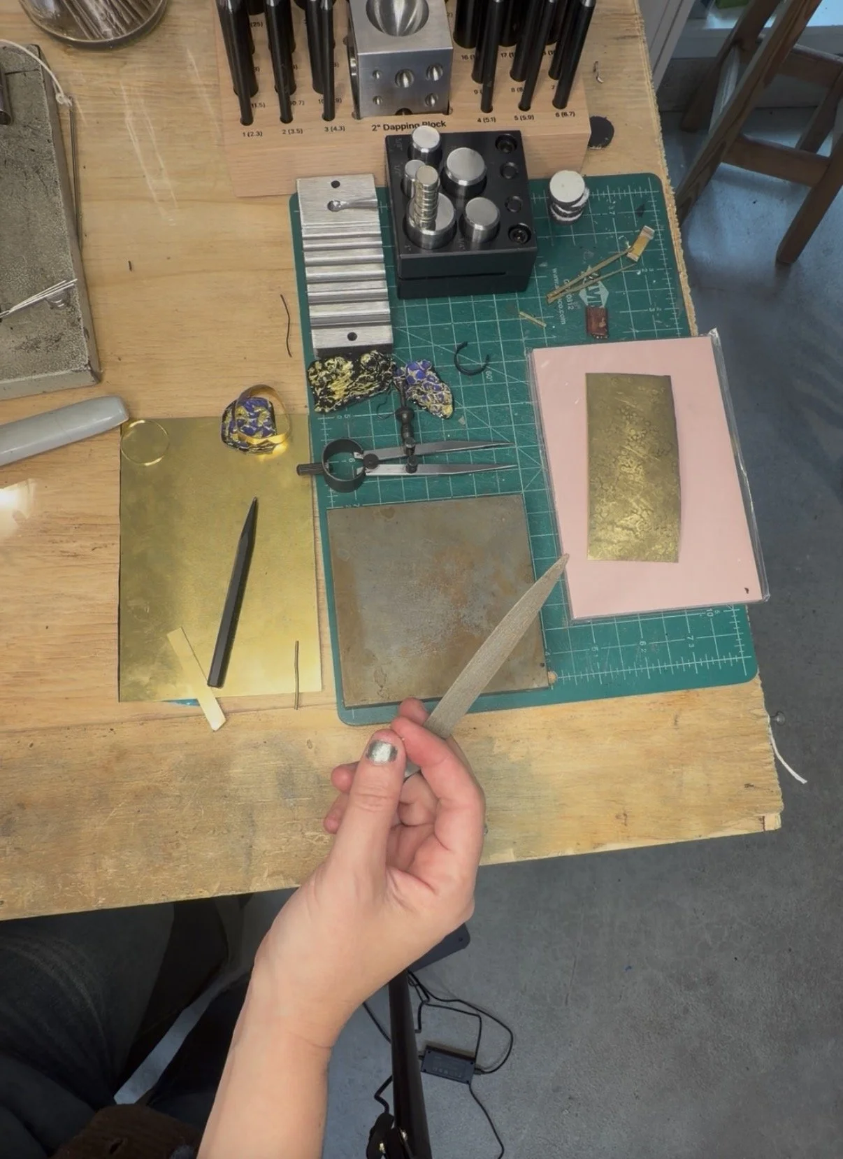 Metalsmithing bench with brass sheet and jeweler tools — Einat Cohen working on New Metal line at Frog Aspect Brooklyn studio