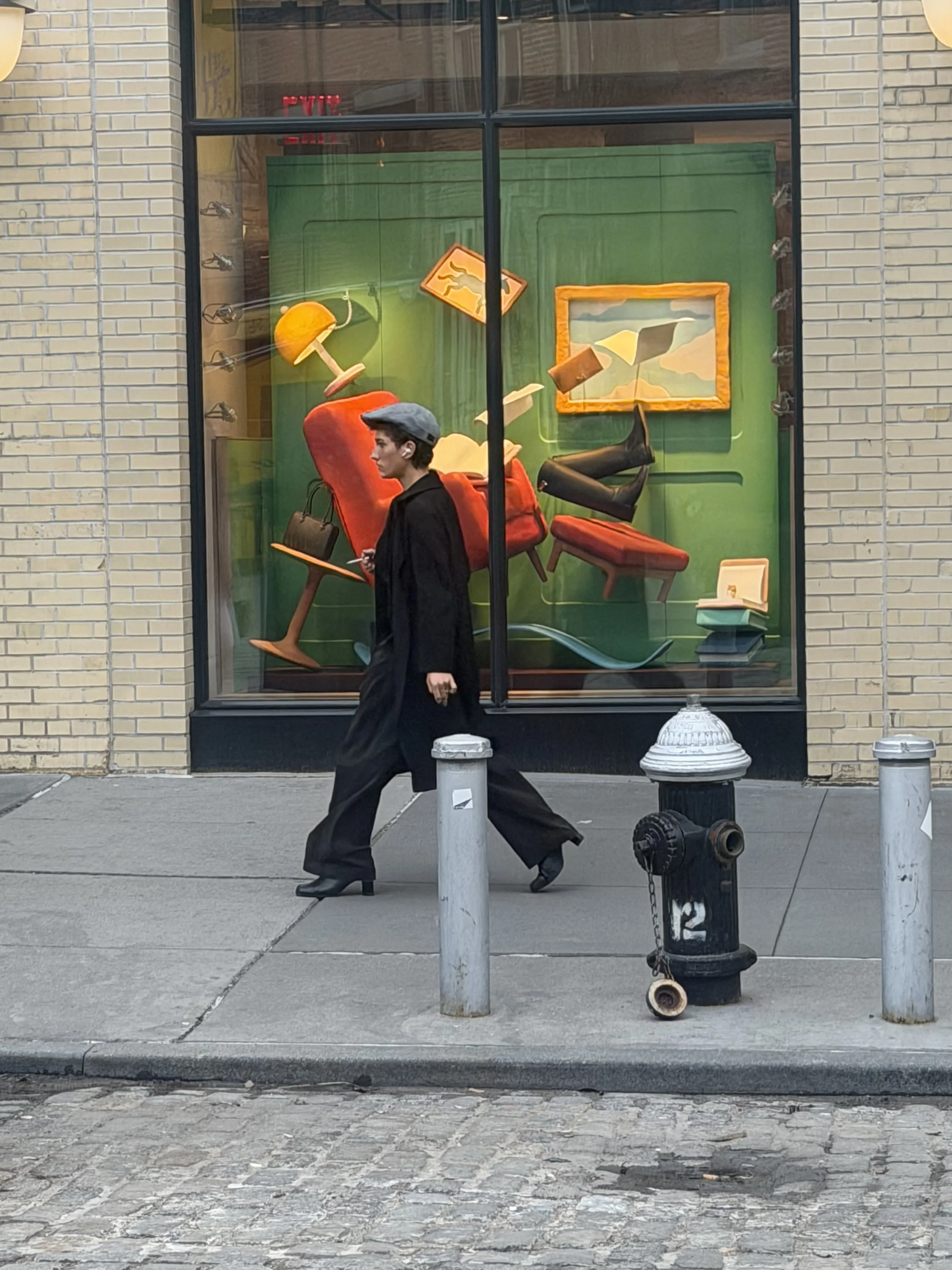 Woman in black coat and beret walking past a New York City shop window displaying floating furniture — street photography by Einat Cohen of Frog Aspect Brooklyn