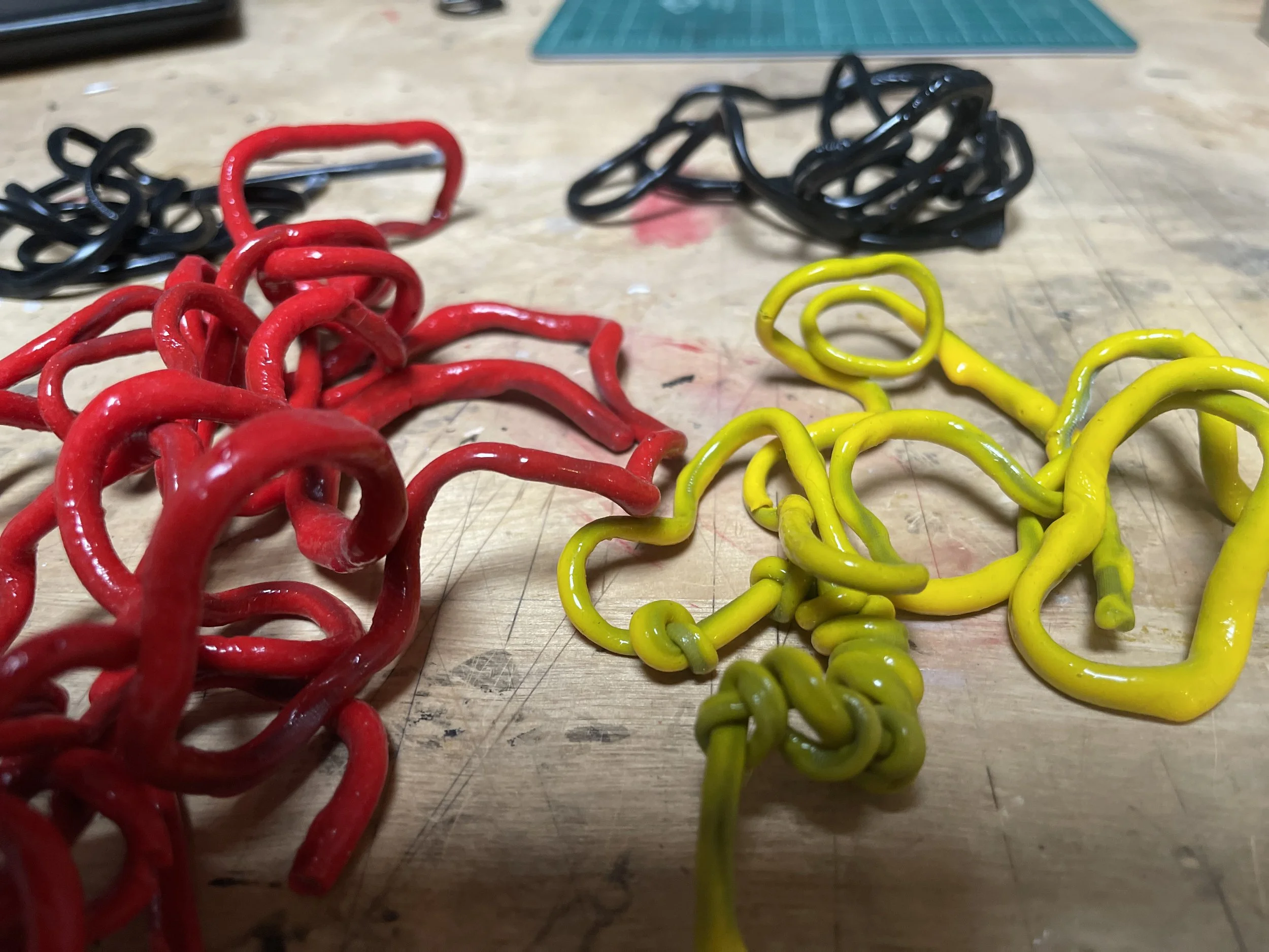 Spandex cord coated in rubber in red yellow and black on worktable — raw material used in handmade Frog Aspect art jewelry Brooklyn