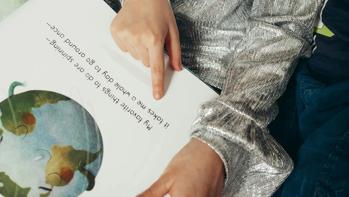 A person pointing at a book or paper that features a puzzle image of the Earth and the text, "My favorite thing to do is learn to go around space."