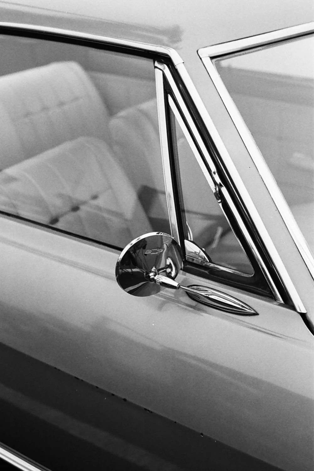 Close-up of a vintage car's side mirror and window with a reflection of the interior seats.