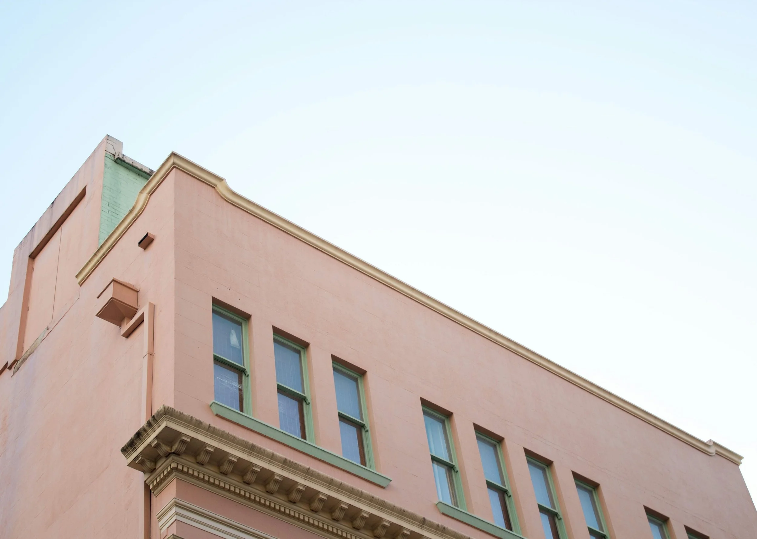 A pink building with green window frames and a decorative cornice, set against a clear blue sky.