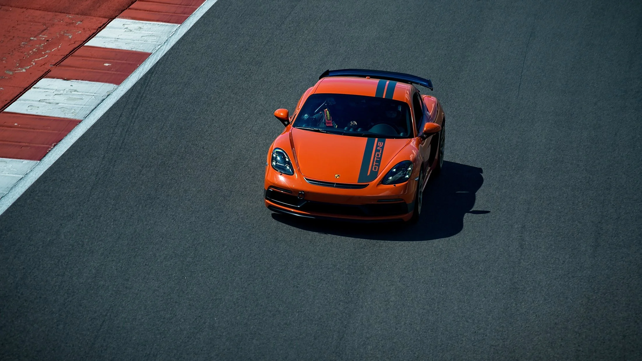 An orange sports car with black racing stripes and a rear wing, speeding on a race track.