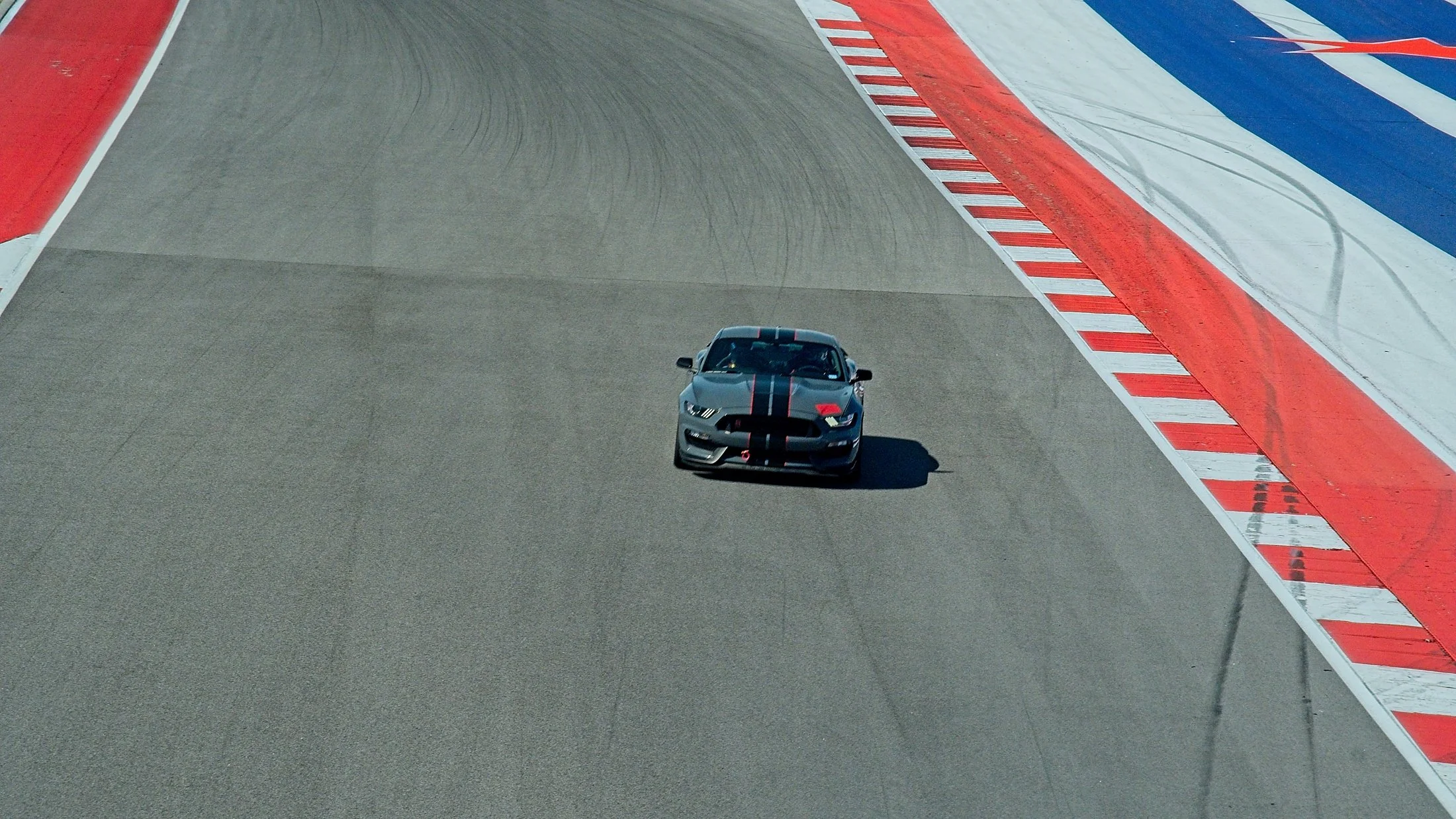 A race car on a racetrack with red, white, and blue painted curbs.