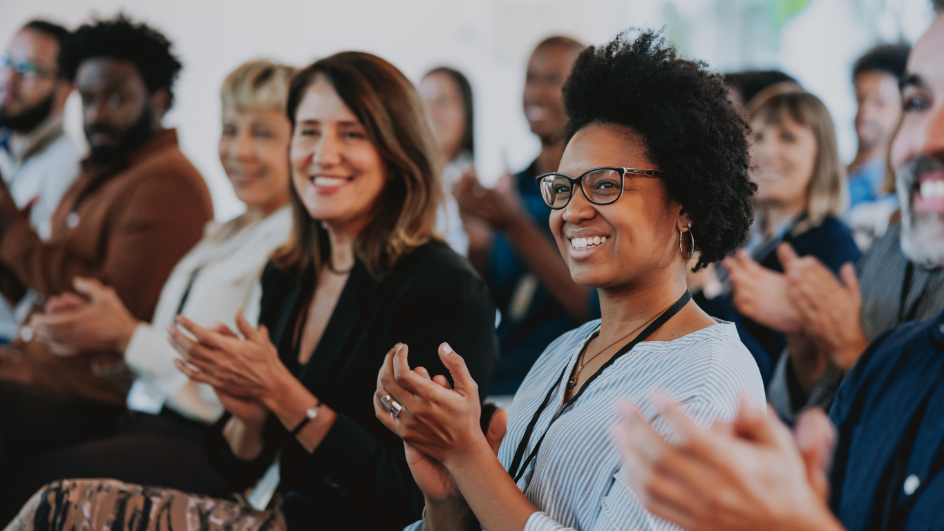 Diverse audience smiling and applauding during a professional workshop or leadership seminar.