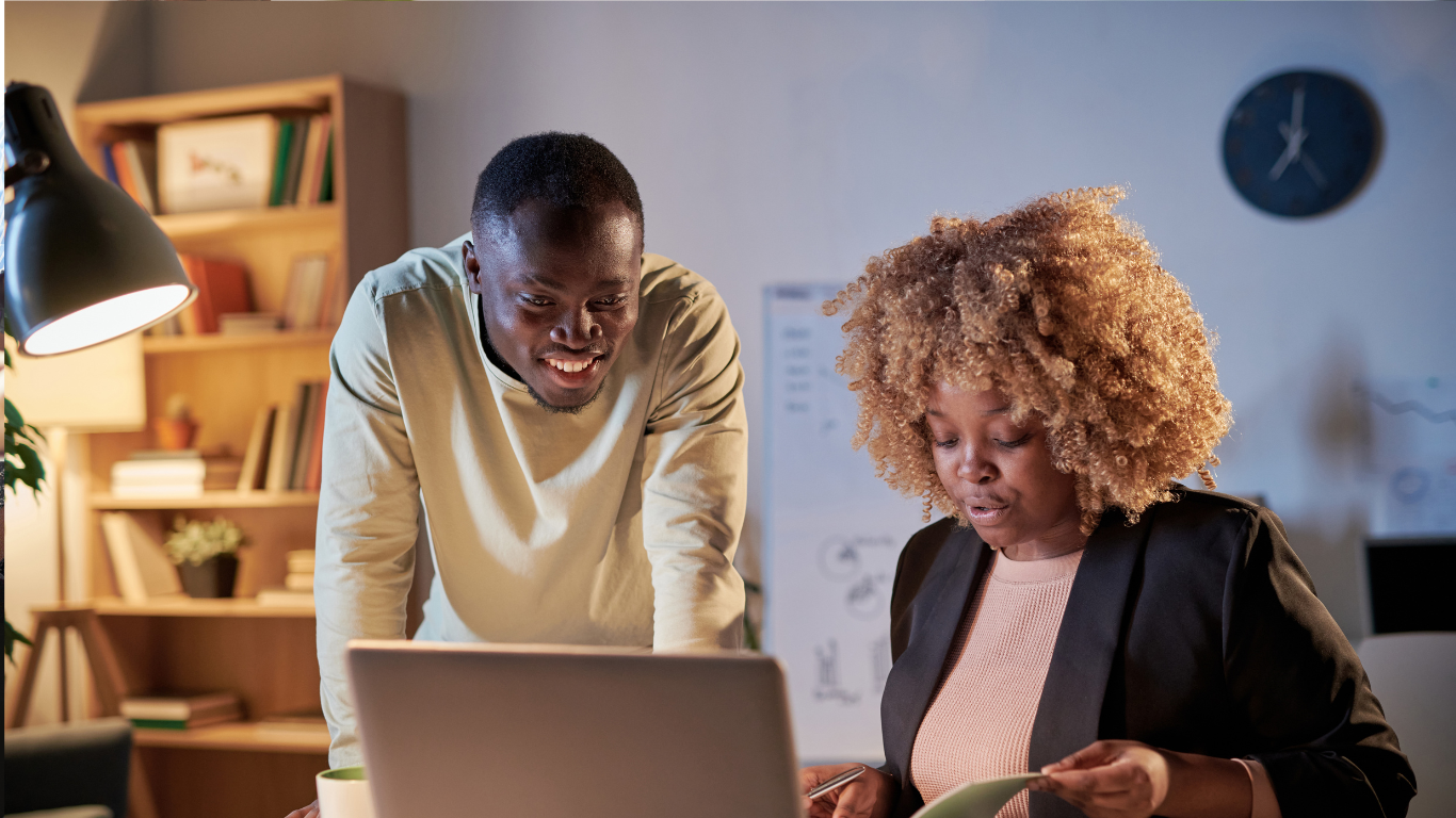 Two persons of color discussing sessions notes together at a laptop during a focused coaching session in an office.
