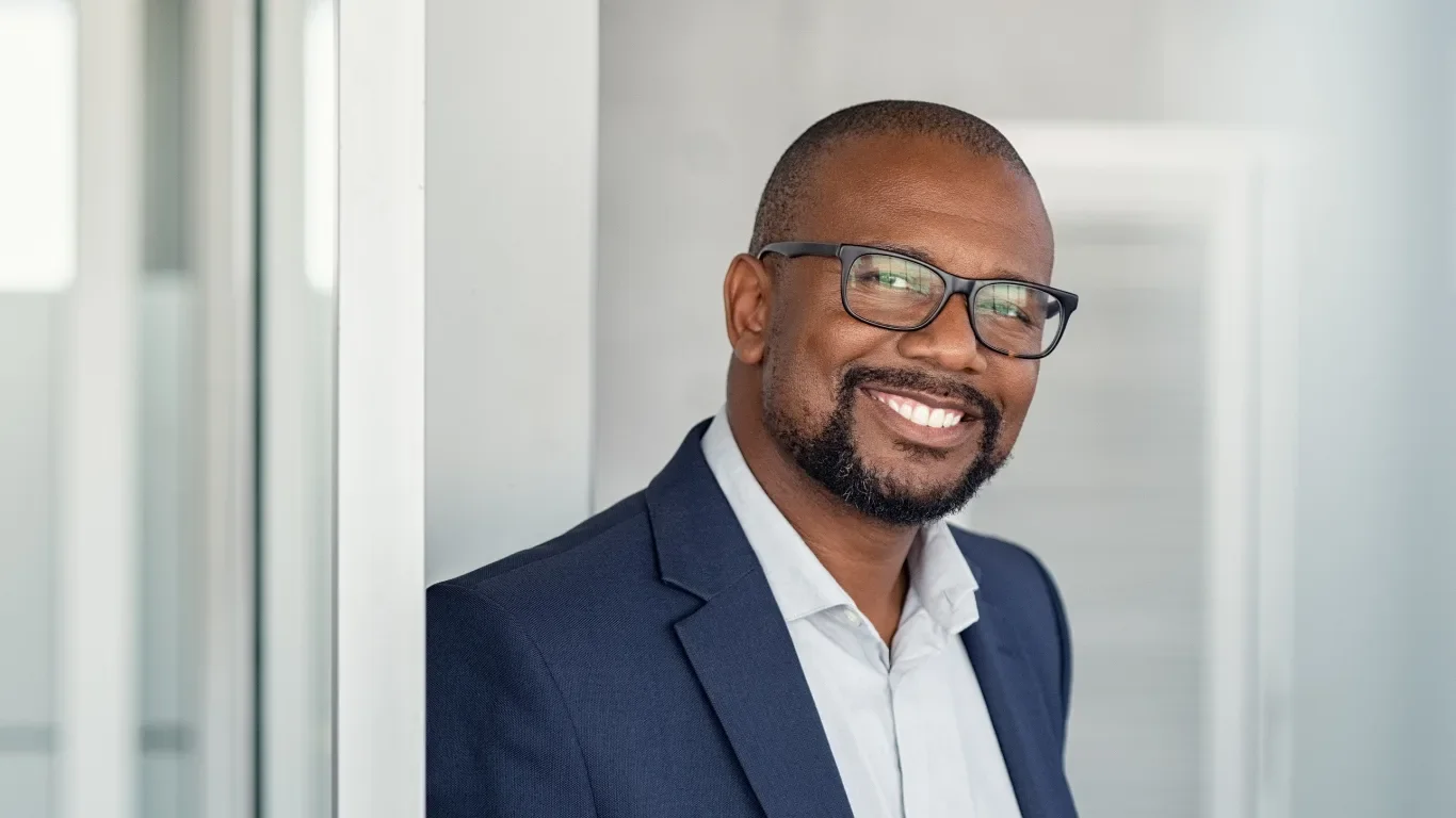 Confident business leader in glasses and navy blazer smiling in a modern office environment