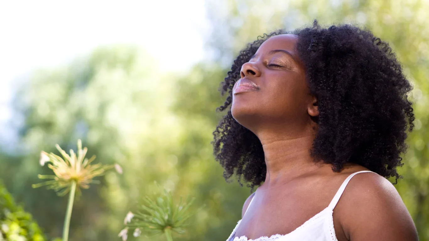 Woman with eyes closed breathing deeply outdoors in a green natural setting symbolizing healing and sustainability