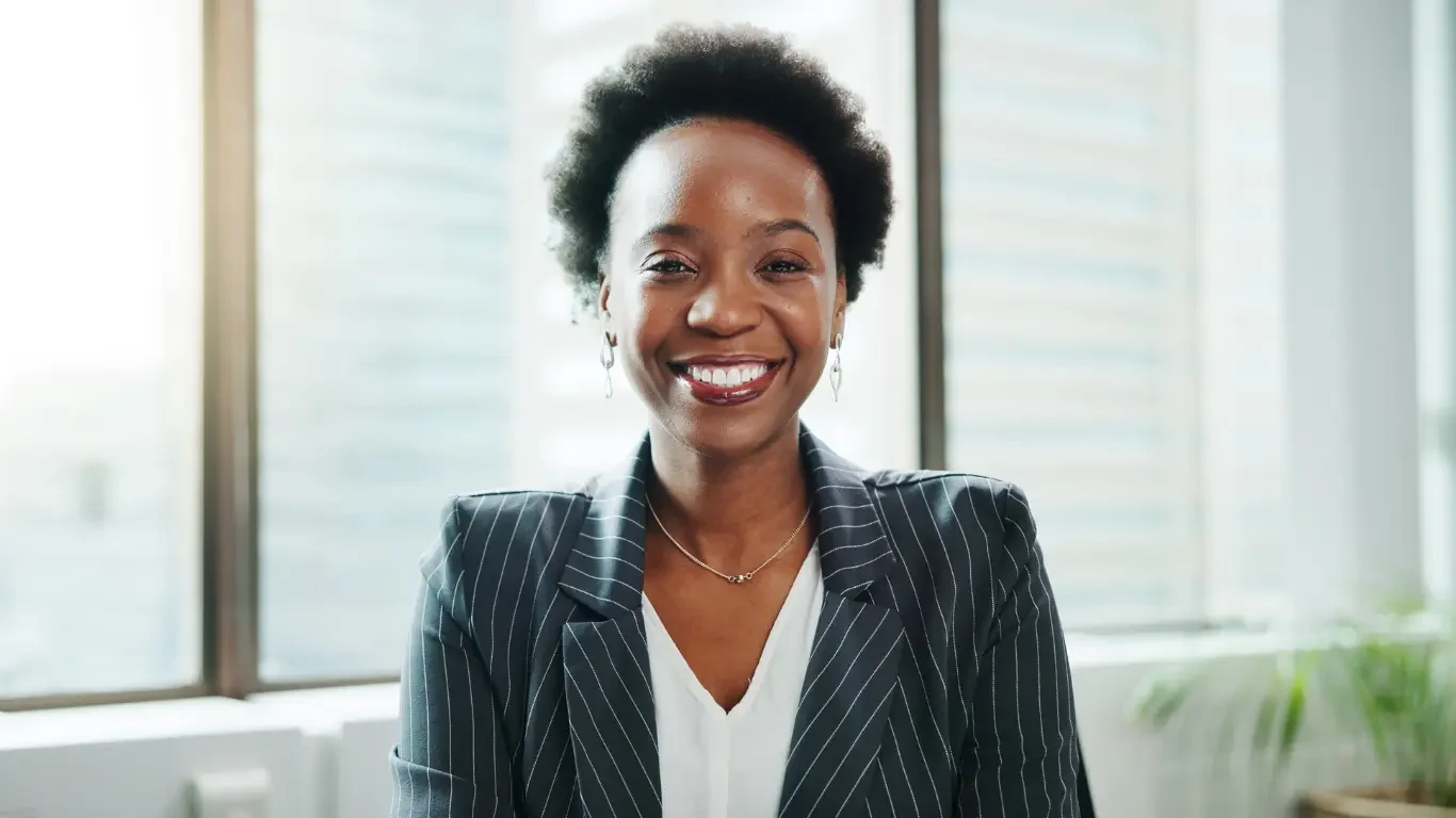 Professional woman in a modern office smiling confidently, symbolizing reflective, purpose-driven leadership grounded in clarity and self-awareness.
