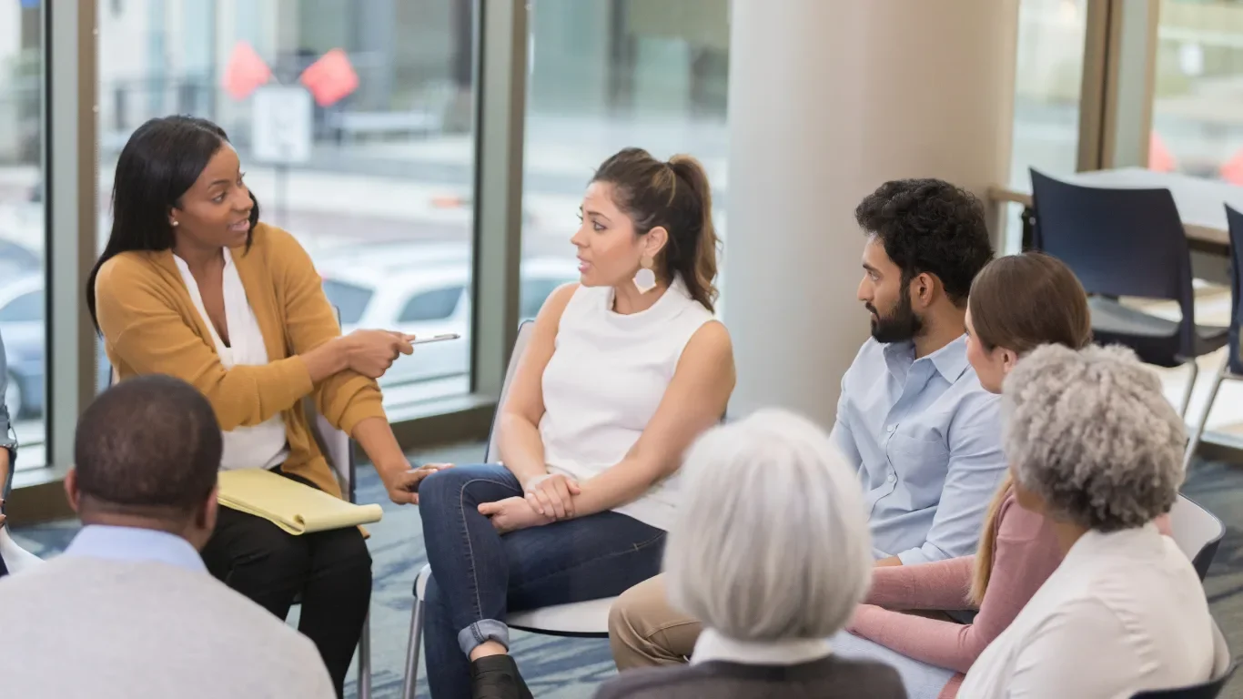 Facilitator leading a diverse small group discussion in a bright meeting space