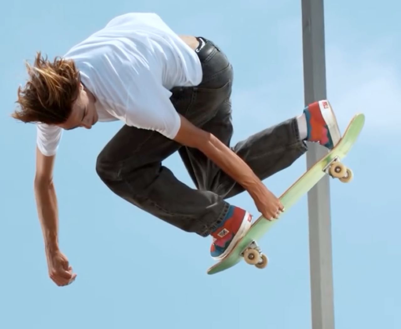 Skateboarder performing a trick on a skateboarding ramp, mid-air with clear blue sky background.