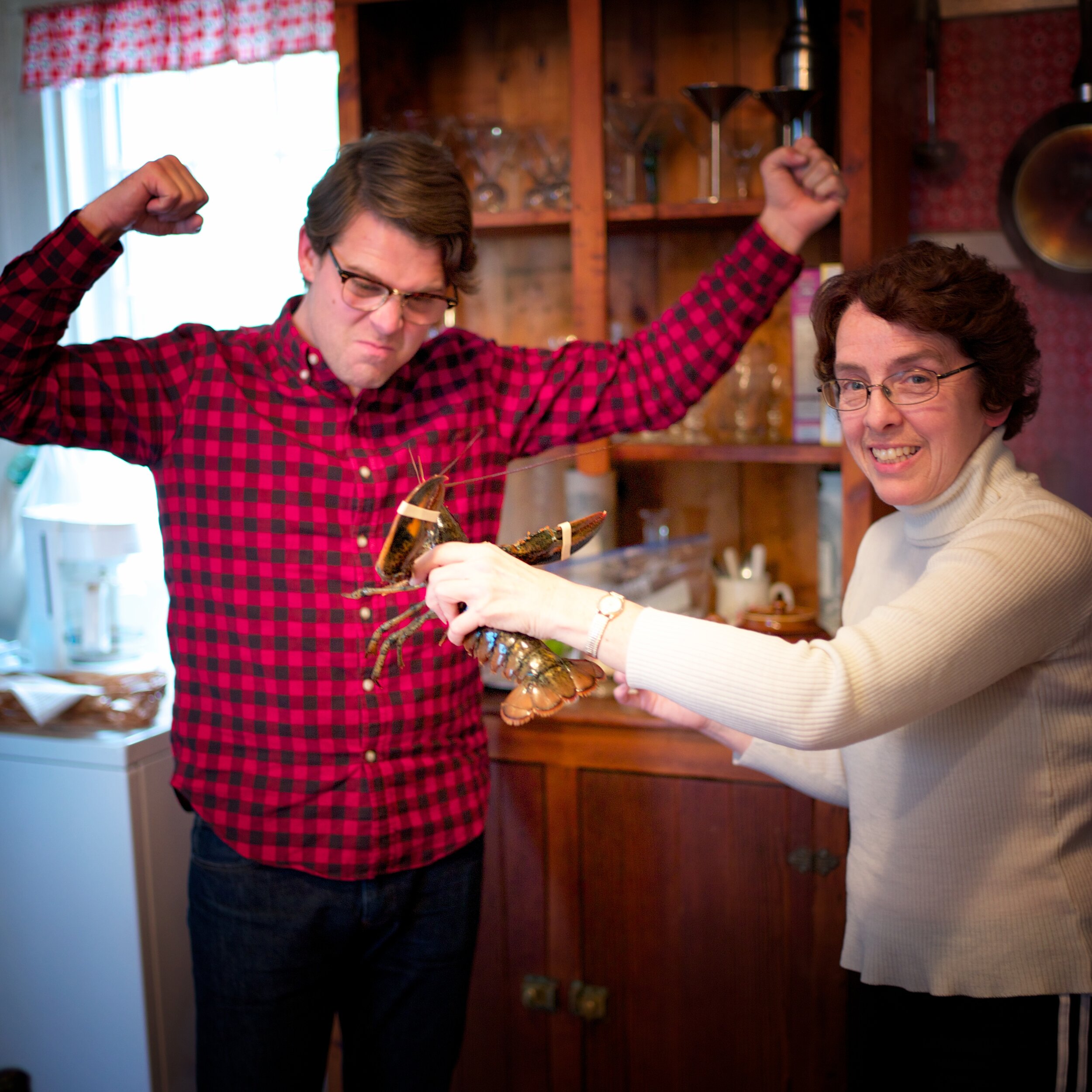 Fr. Matthew Larsen picks a fight with a lobster, held by Miss Susan Harris, Petite Riviere, Nova Scotia