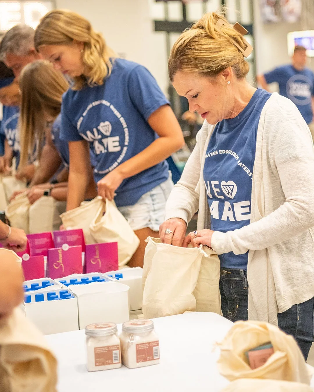 People wearing matching blue T-shirts packing food into bags at a community service event.