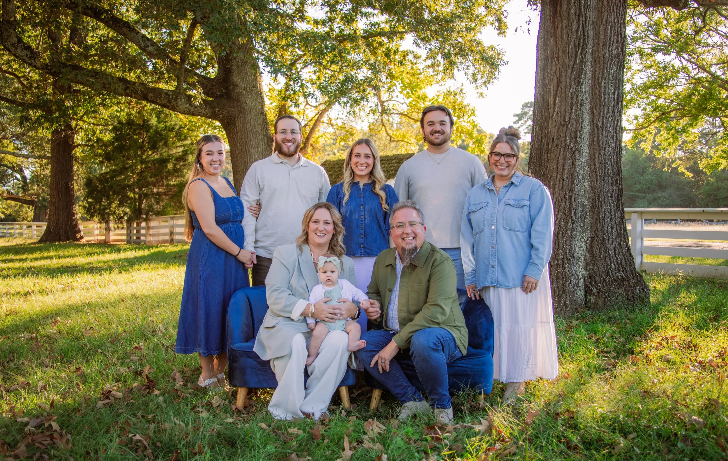 Pastor Stu and his wife, Tab, seated outdoors with their family, smiling together beneath large trees in a park setting, reflecting a warm and relaxed family moment.