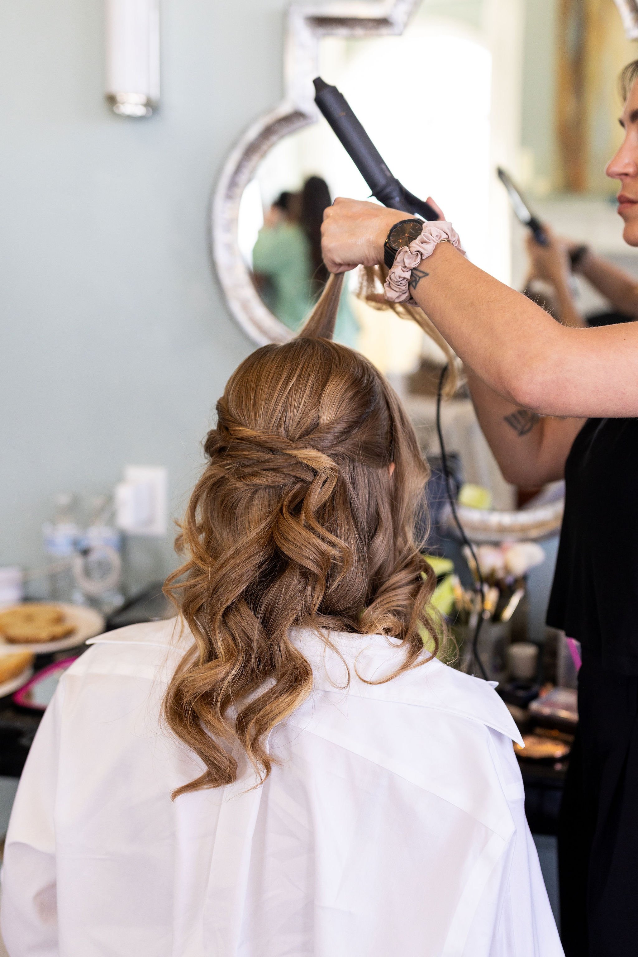 A hairstylist curling a woman's long, wavy hair in a salon.