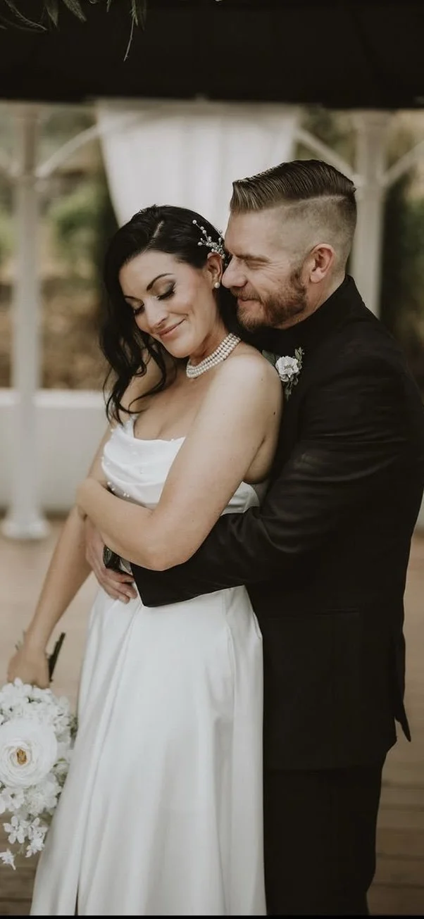 A bride and groom sharing a tender moment at their wedding, with the groom hugging the bride from behind.