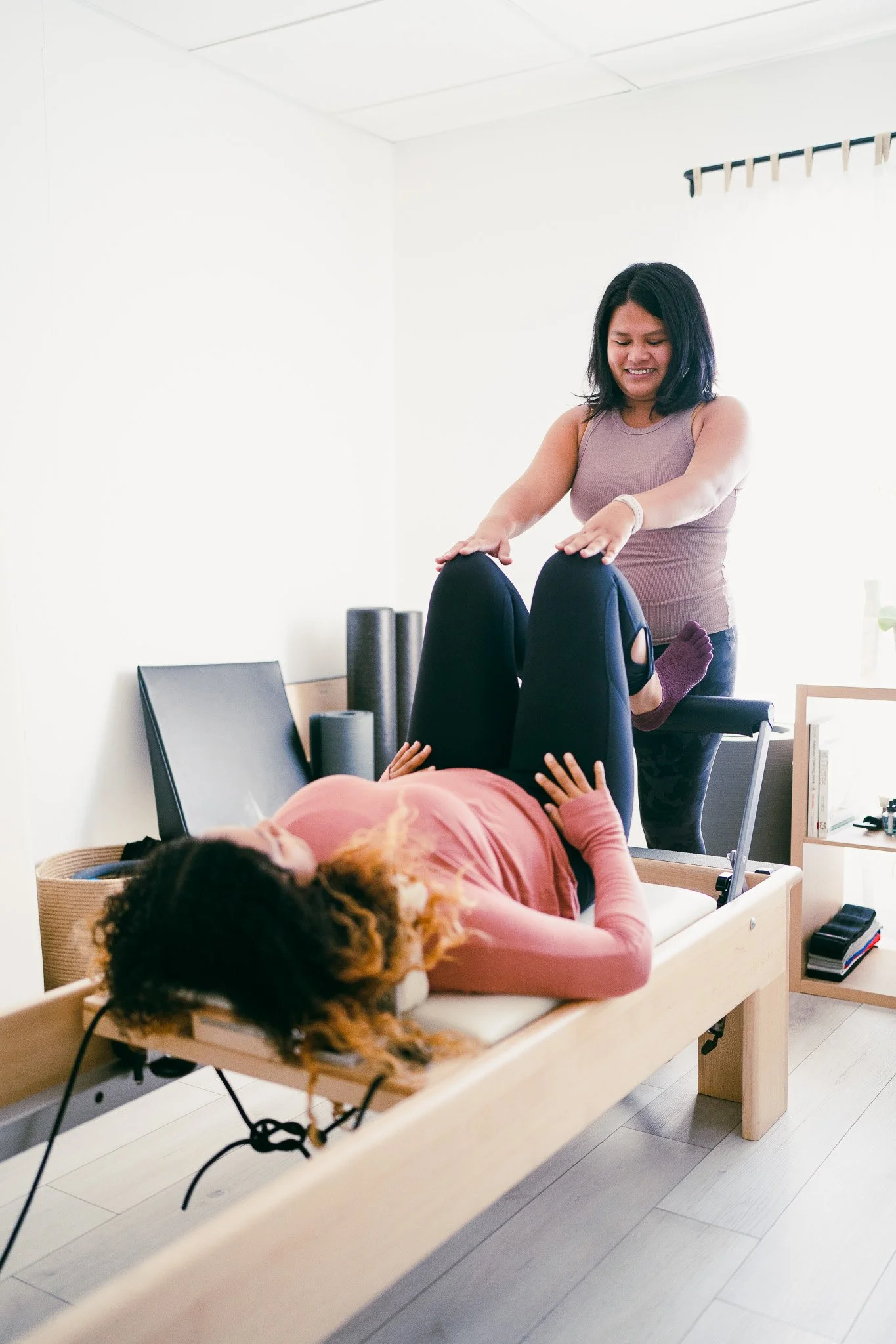 julie teaching a private student on the pilates reformer equipment adjusting their knees in footwork alignment