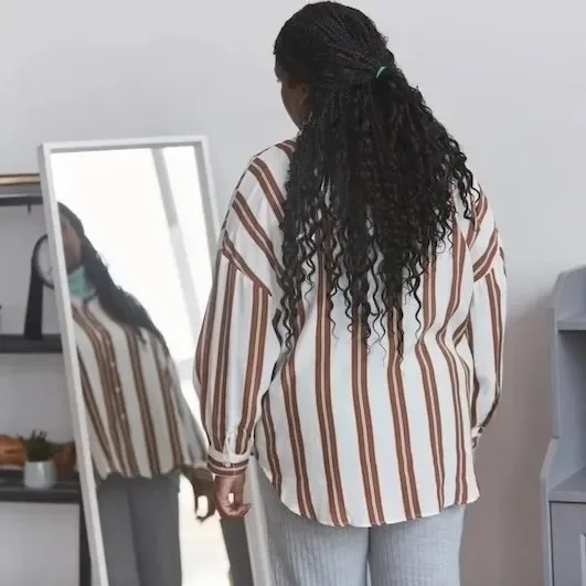 Black genderfluid person with textured hair and striped shirt, head tilted in thought. Therapy for body image and disordered eating for gender-expansive folks.