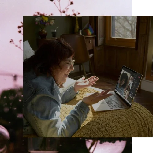 Person lying on their stomach on a bed, smiling during a video group therapy call. Online body image support groups for connection in California.