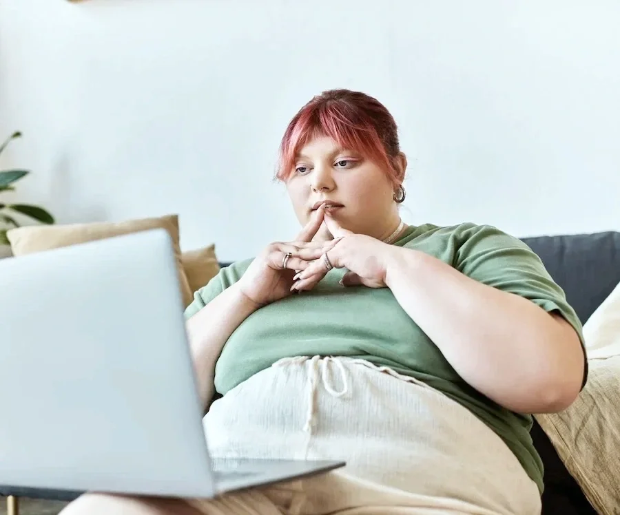 Person at a laptop with clasped hands and a reflective expression.