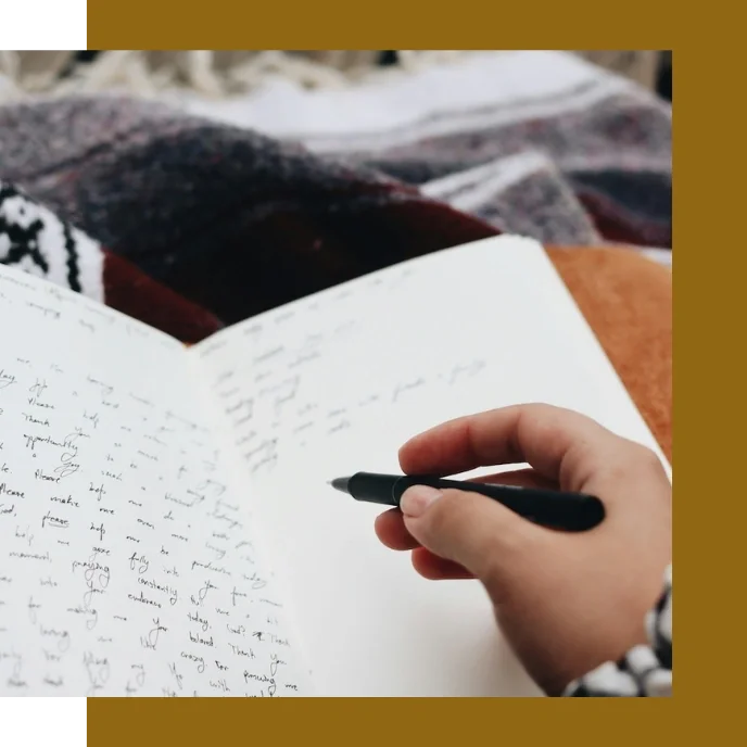 Close-up of a hand writing in a journal with a blanket over legs. Processing weight stigma and finding self-trust through fat-positive therapy.