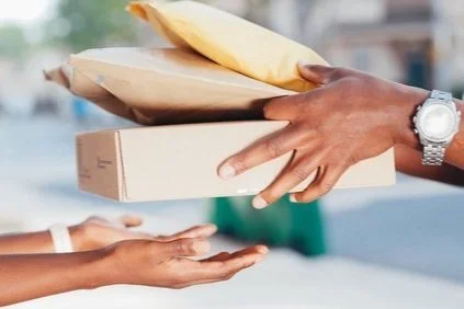 Person handing over packages and envelopes to another person on the street.